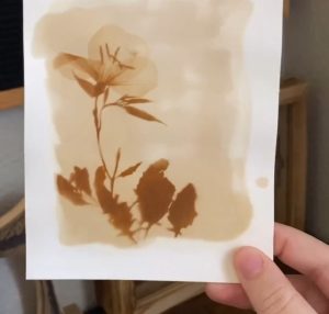 Hand holding dark brown print of flower on light brown background.